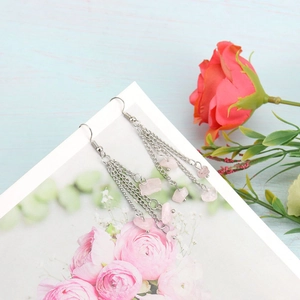 Close-up of dangling silver chain earrings with pink crystal stones on floral background