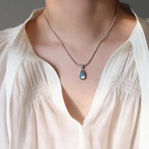 Detailed view of sea blue water-drop pendant on silver snake chain worn by a model