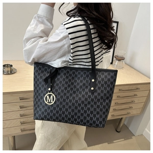 Classic black monogram tote bag with metallic M-logo charm shown in a lifestyle setting