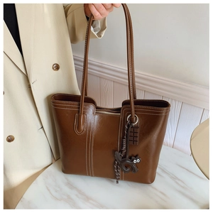 Detail of dark brown leather tote bag with white contrast stitching and cat charm decor