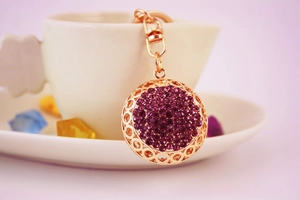 Close-up of golden hollow metal keychain pendant with inlaid purple rhinestones
