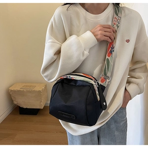 Detail of black crossbody shell bag featuring a colorful floral embroidered wide strap