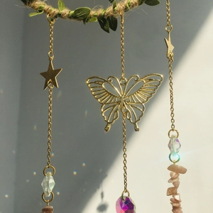Detail of metal moon wind chime with golden butterfly and purple crystal reflecting rainbows