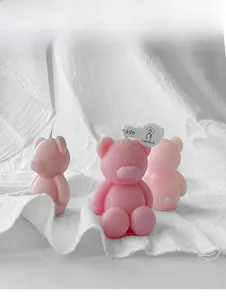 Close-up of cute pink bear scented candles with decorative tags on white fabric