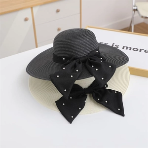 Detail of wide brim straw hats in black and beige with large pearl bow decorations