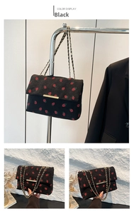 Detail of black corduroy shoulder bag featuring red strawberry prints and gold chain strap