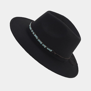 Detalle de sombrero fedora negro con banda de cuentas turquesas sobre fondo gris