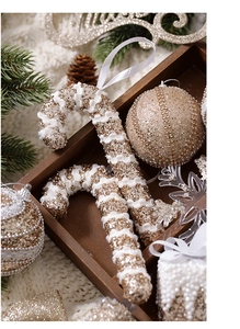 Detail of glittery champagne candy cane ornaments and golden bauble in a rustic wooden tray