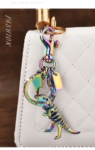 Rainbow metal dinosaur skeleton keychain hanging on a white quilted leather handbag