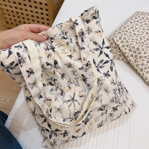 Close-up of beige canvas tote bag with black ink leaf pattern and branded fabric label