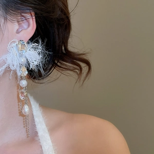 Close-up of elegant white feather earrings with crystal pearls and metal chain tassels