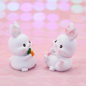 Detail shot of two cute white resin bunny figurines with a carrot on pink bokeh background
