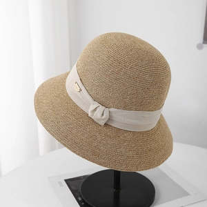 Gros plan détaillé d'un chapeau de paille avec ruban beige, noeud et plaque de logo dorée