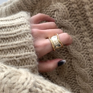 Irregular golden wide-surface ring styled on a hand with a beige knit sweater background
