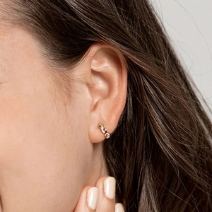 Close-up of a model wearing minimalist gold braided hoop earrings on a light gray background
