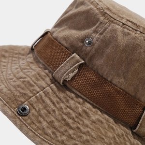 Detail of a rugged brown tactical bucket hat with distressed cotton fabric and metal buckle