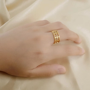 Gold hollow cross pattern ring on model's hand with elegant silk background