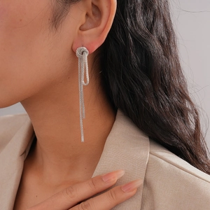 Close-up of silver knot chain tassel earrings worn by a model in a beige suit