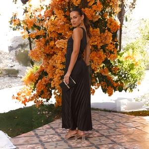 Detail of elegant black one-shoulder pleated maxi dress against a floral outdoor backdrop