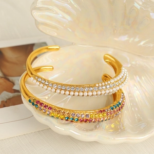Elegant gold open cuff bracelets with pearls and colorful zircons on a shell base