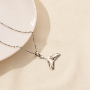 Detailed view of silver whale tail pendant necklace on textured beige fabric