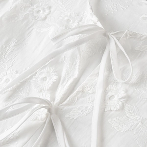 Detailed view of white floral embroidery and delicate tie-up design on cotton fabric