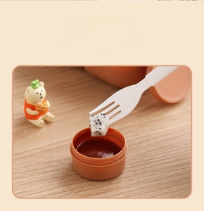 Close-up of a portable orange sauce container with a white fork for bento lunch boxes