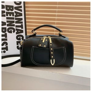 Détail du sac Boston noir avec ferrures dorées, surpiqûres blanches et poignée supérieure