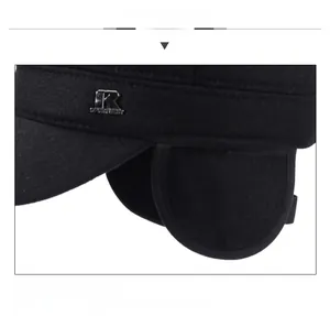Detail view of winter black flat cap featuring foldable ear flaps and metal letter logo