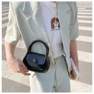 Close-up of black glossy mini bag with gold chain strap on a street crossing background