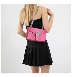 Detail of pink croc-effect crossbody bag with silver chain and crystal buckle on a model