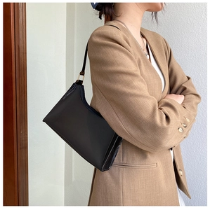 Detail of a black minimalist PVC shoulder bag with golden metal buckle and sleek stitching