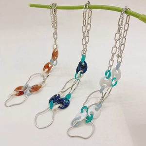 Three colorful acrylic pig nose chain necklaces hanging on a green branch in a white studio