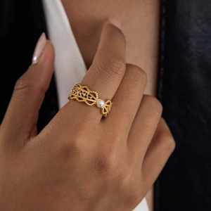Close-up of a gold hollow-out ring with a white pearl and zircon on model finger