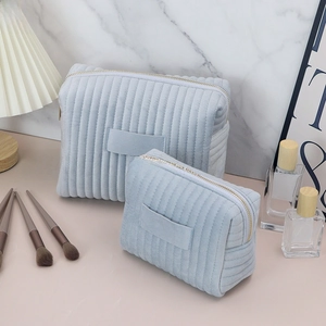 Macro detail of large and small light blue quilted velvet cosmetic bags with gold zippers