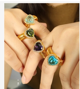 Close-up of four colorful heart-shaped crystal rings with gold spiral bands for women