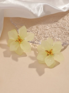 Detail of light yellow matte flower earrings with golden core on a white fabric background