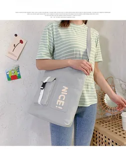 Detail of light grey canvas crossbody bag featuring NICE lettering and buckle pocket