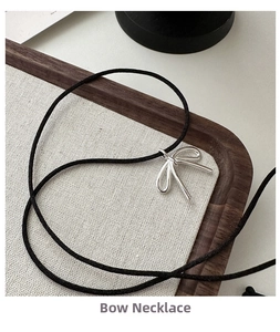Close-up of a s925 silver bow pendant on a black cord necklace in a linen tray