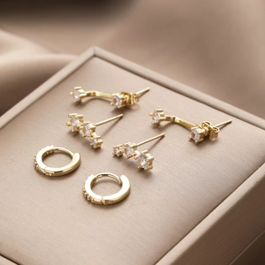 Macro shot of three pairs of gold zircon stud earrings on champagne velvet and silk