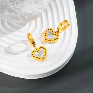 Macro detail of gold-plated hollow heart pendant earring on a white wavy tray