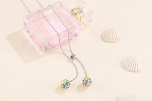 Silver Y-necklace with multi-color crystal paved ball pendants on a perfume bottle