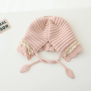 Detail of pink knitted baby bonnet featuring cream lace trim and leaf ties