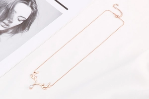 Détail du collier bois de cerf or rose avec un zircon goutte sur un tissu blanc