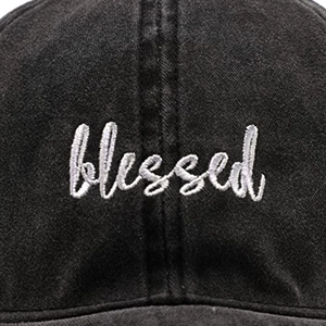 Détail macro de la broderie blanche blessed sur une casquette en coton lavé noir