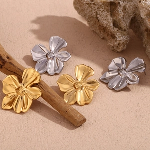 Detailed view of 18K gold and silver flower stud earrings on a textured stone surface