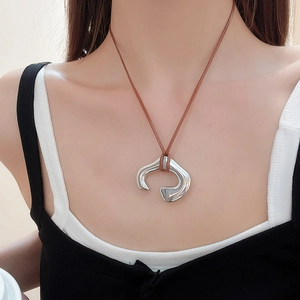 Detailed view of the abstract irregular silver C-shaped pendant on a brown leather cord