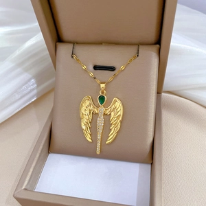 Detailed shot of gold angel wing necklace with green gemstones in a beige jewelry box
