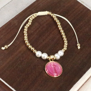 Detail of adjustable woven bracelet with gold beads, pearls, and pink religious pendant