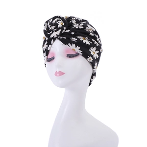 Detail of black turban hat with white daisy floral print and front knot design on a mannequin